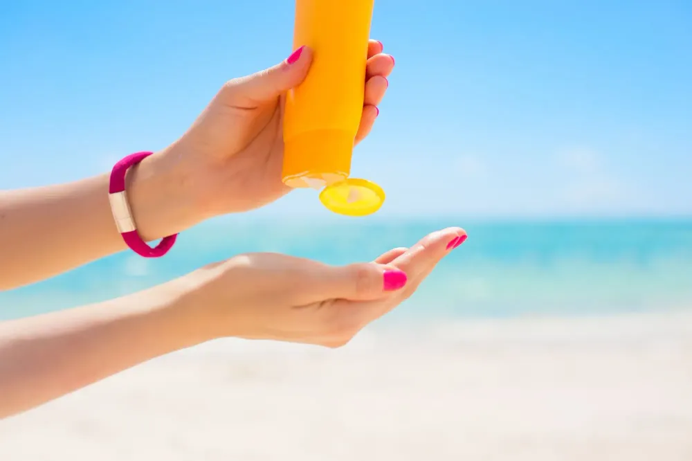 Close up of person squeezing sunscreen from an orange bottle into their open hand at the beach